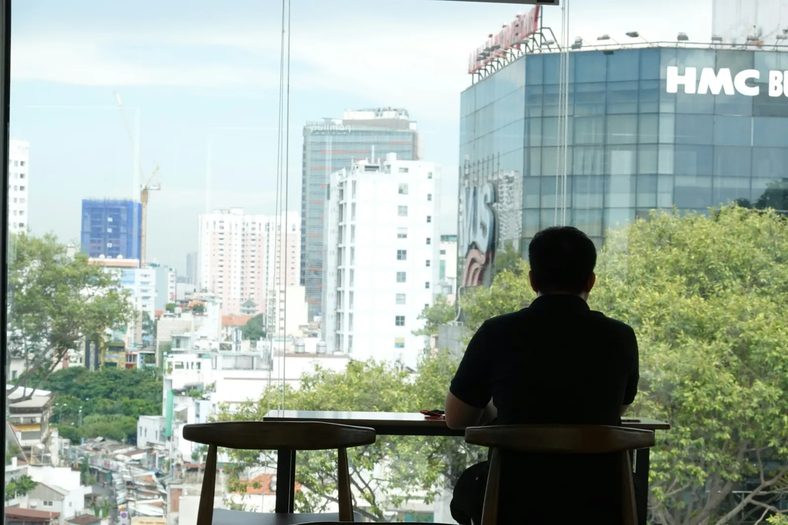 Man vid ett kafébord framför ett fönster med utsikt över kontorshus i Ho Chi Minh-staden