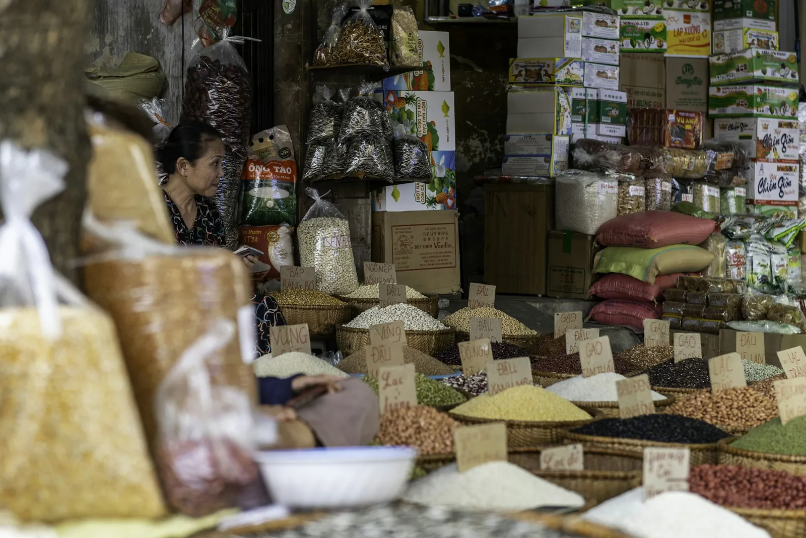 Korgar med bönor, ris och frön med handskrivna prisskyltar i ett marknadsstånd i Hanoi