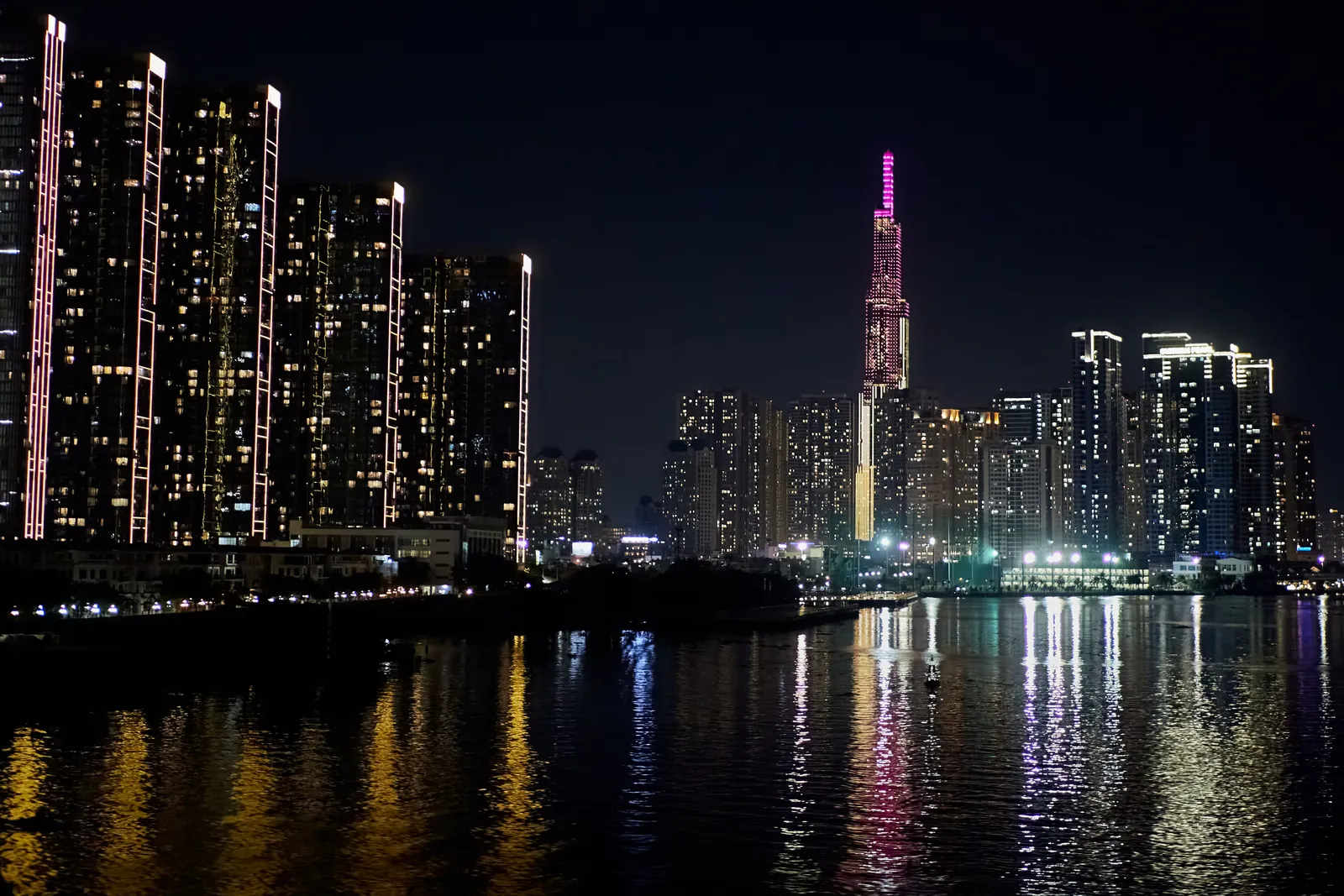 Upplysta bostadshöghus och skyskrapan Landmark 81 som speglas i Saigonfloden i Ho Chi Minh-staden på natten