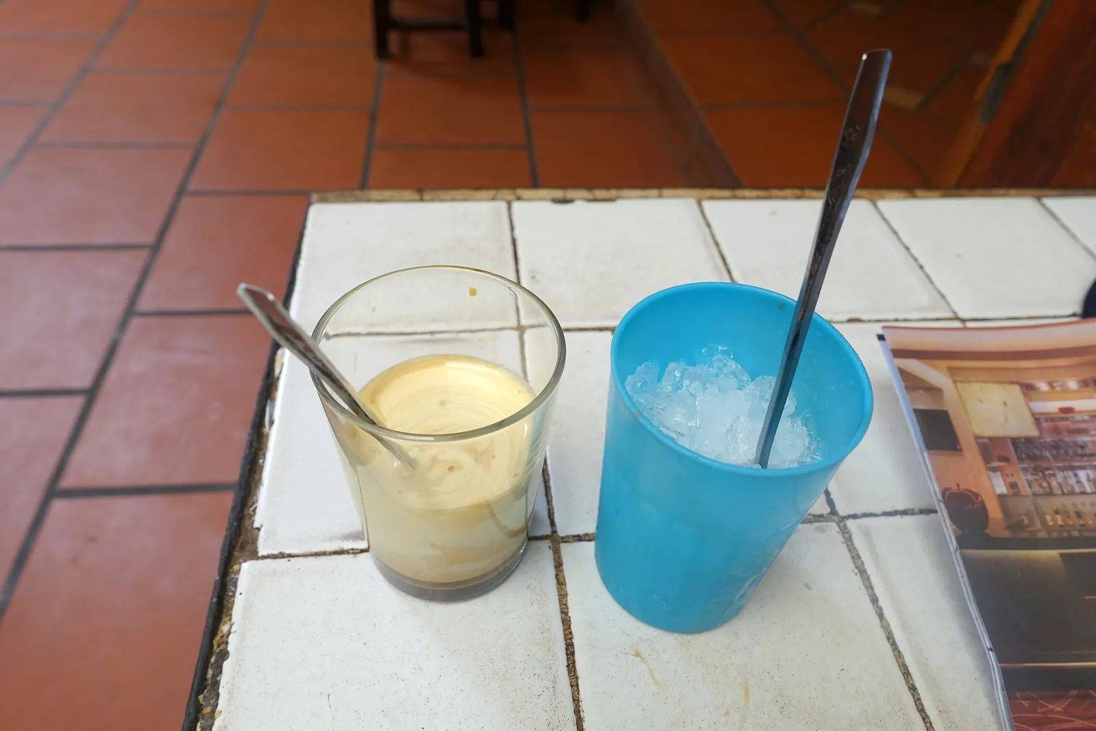 Glas med äggkaffe och en blå mugg med krossad is på ett kaklat bord på Café Giang i Hanoi
