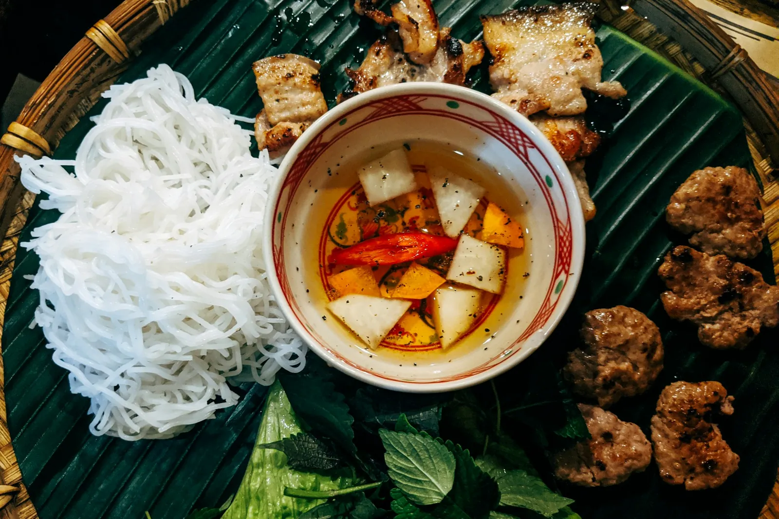 Bun cha med grillade fläskbiffar, fläsksida, risnudlar, örter och doppsås med papaya på bananblad