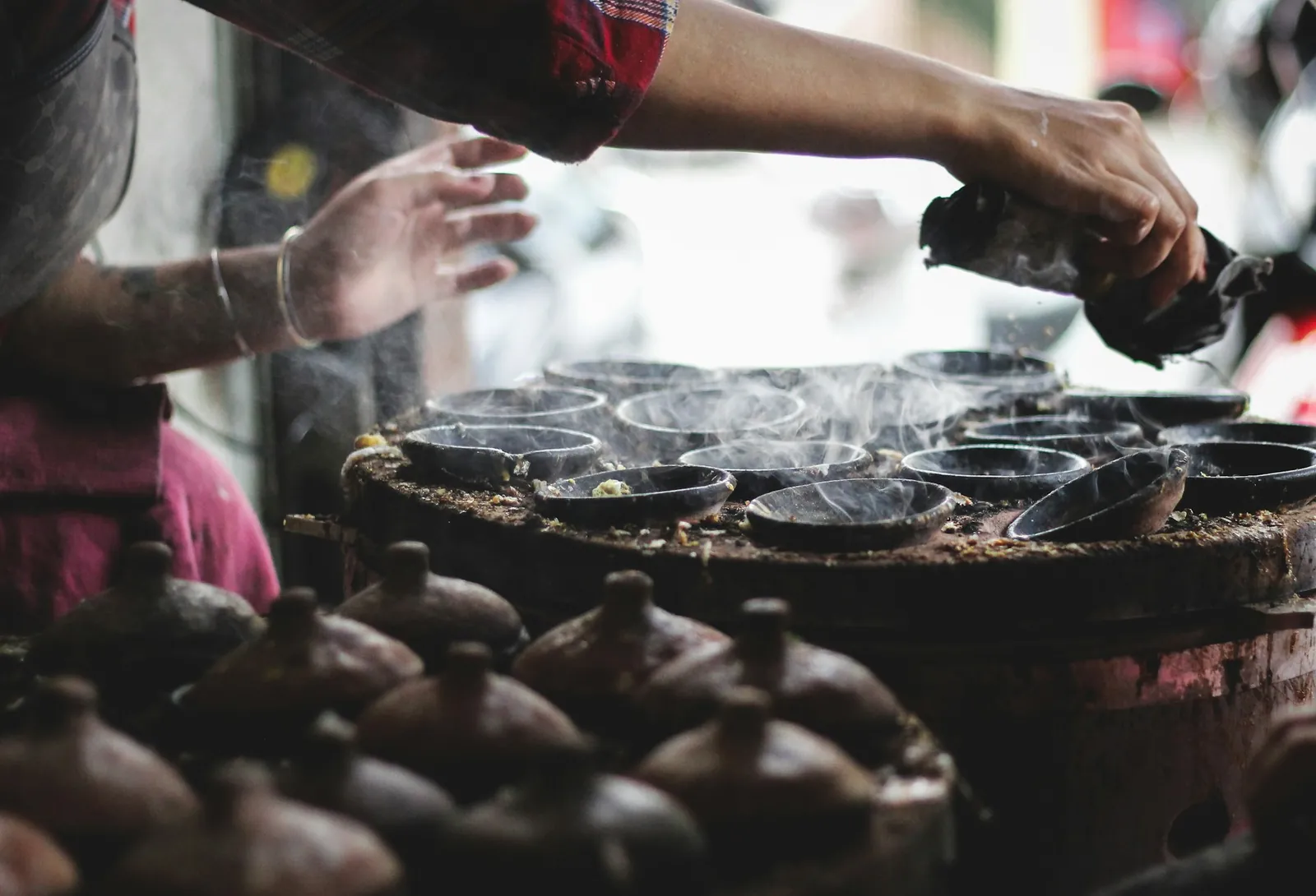 Rykande lerformar på en kolgrill vid ett gatukök där små riskakor gräddas