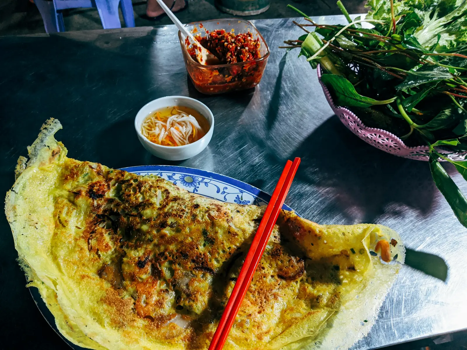 Banh xeo, en krispig risplätt, med färska örter, chili och doppsås på ett gatukök
