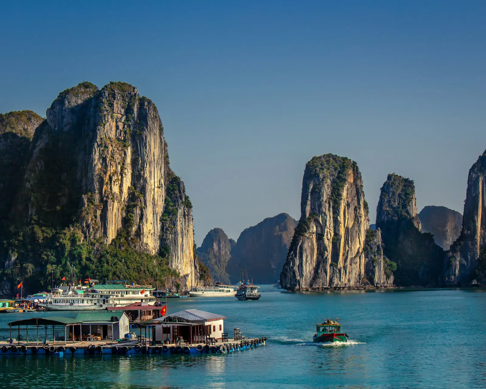 Branta kalkstensklippor, båtar och en flytande by i Ha Long-bukten i klart solljus
