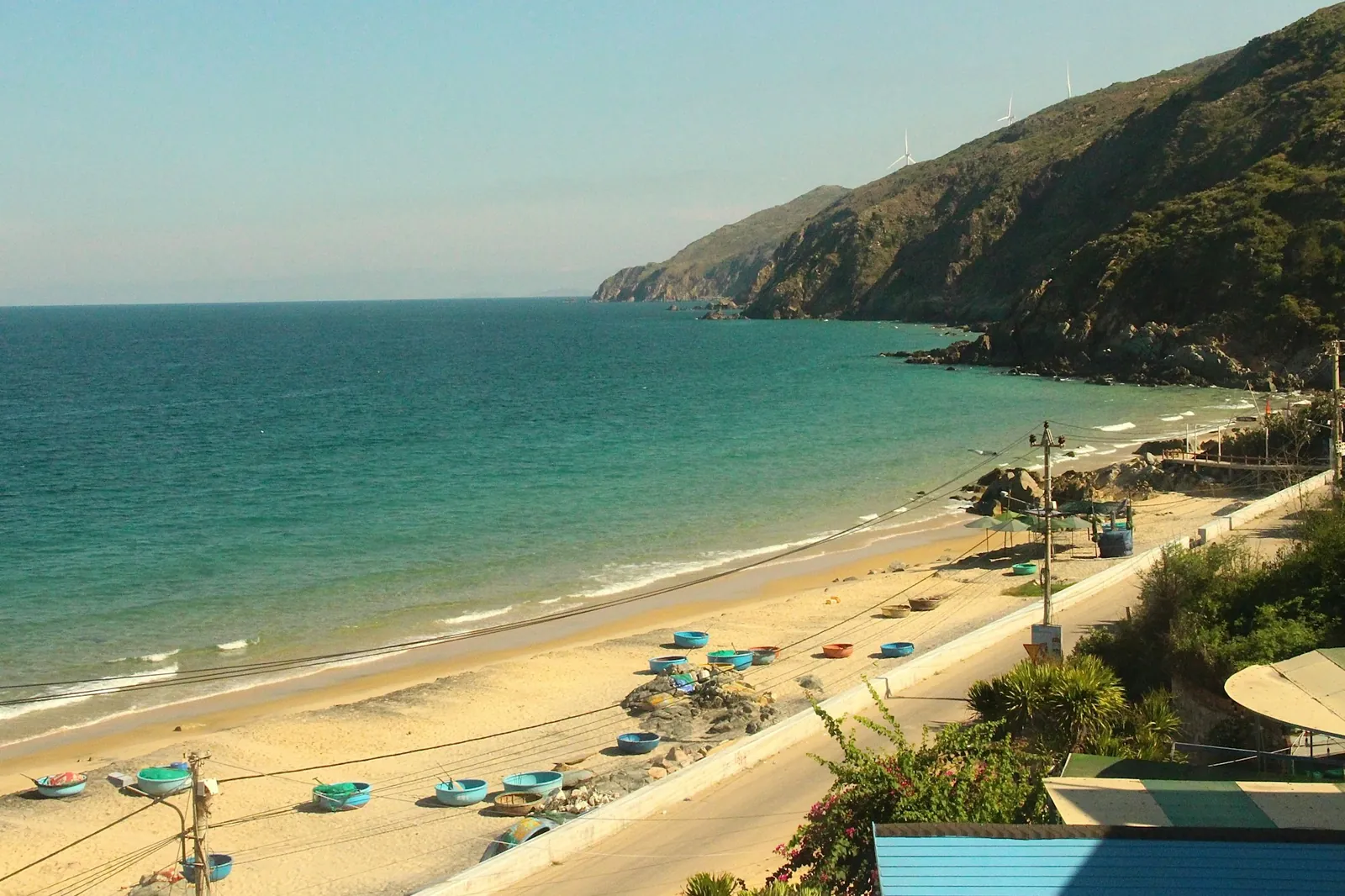 Korgbåtar på en gyllene sandstrand under gröna klippor vid kusten kring Quy Nhon