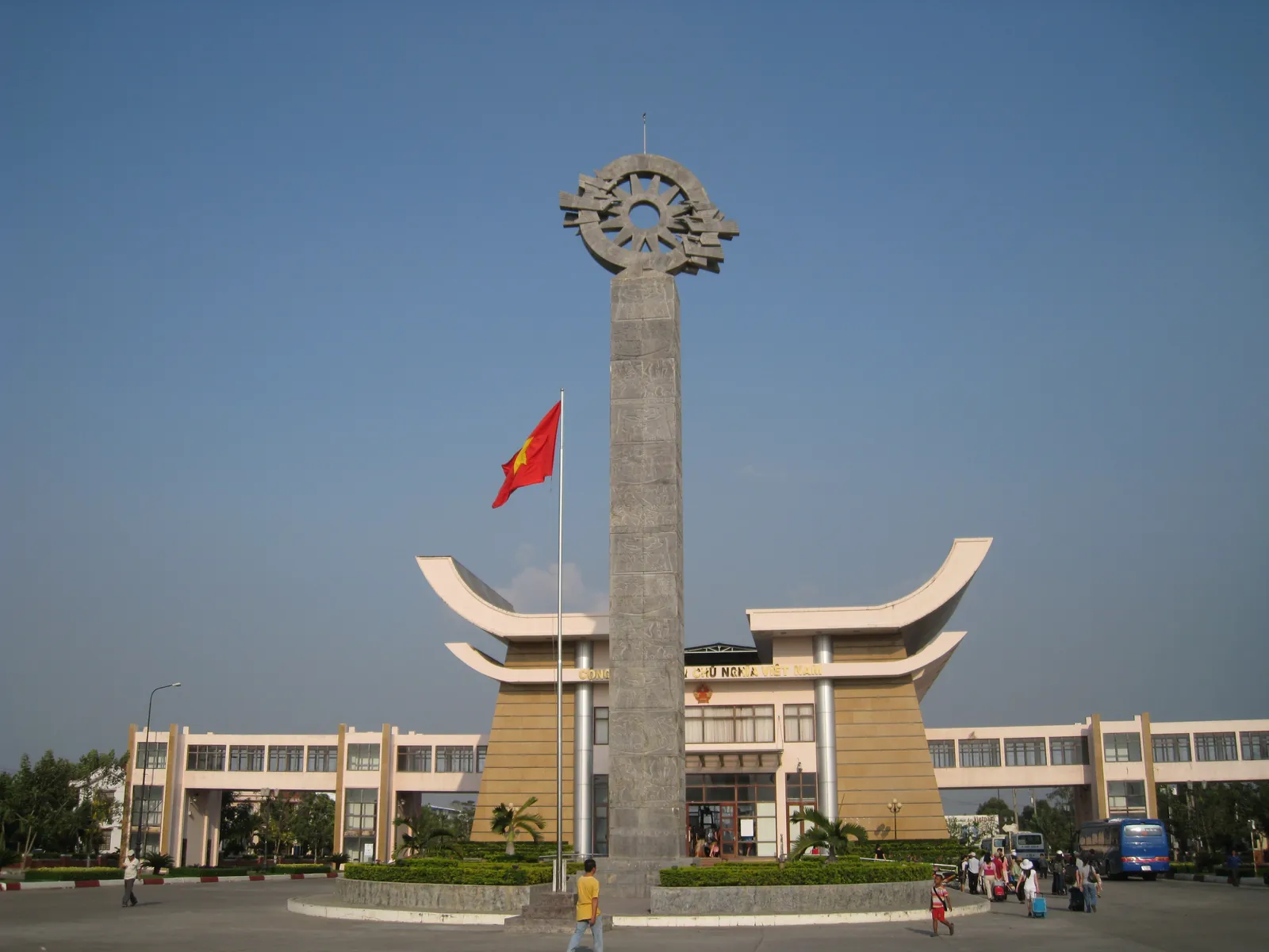 Gränsstationen Moc Bai mot Kambodja med monument, vietnamesisk flagga och resenärer med väskor