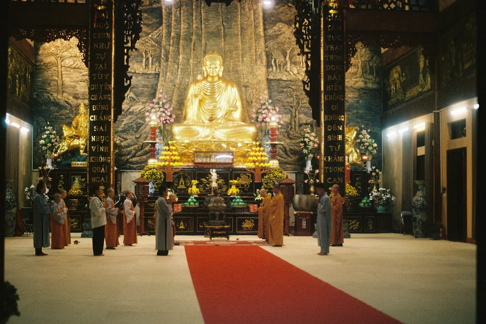 Munkar och besökare framför en stor förgylld Buddhastaty i en vietnamesisk pagod