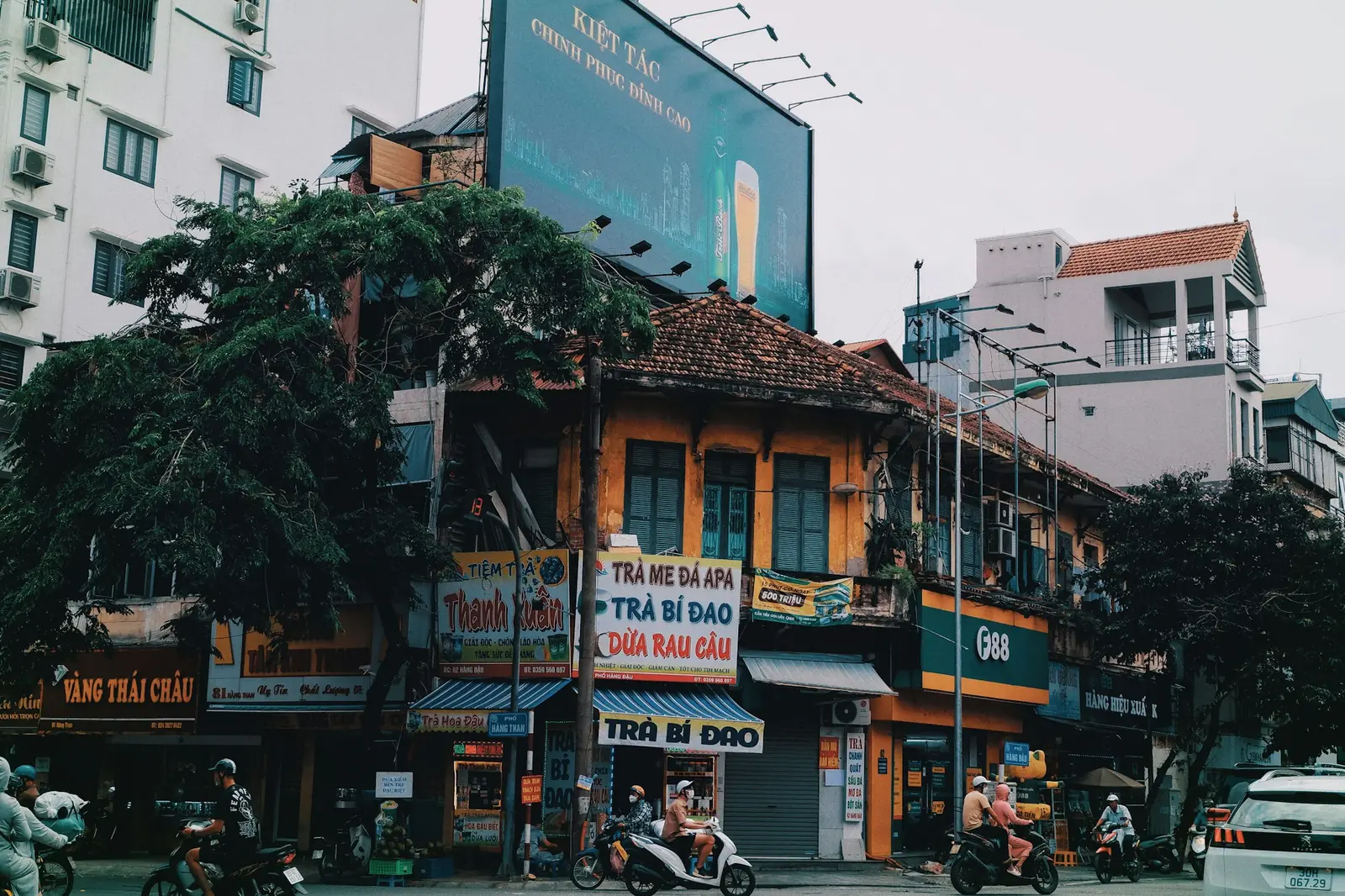 Gammalt gult hus med fönsterluckor, butiksskyltar och mopeder på en gata i gamla kvarteren i Hanoi