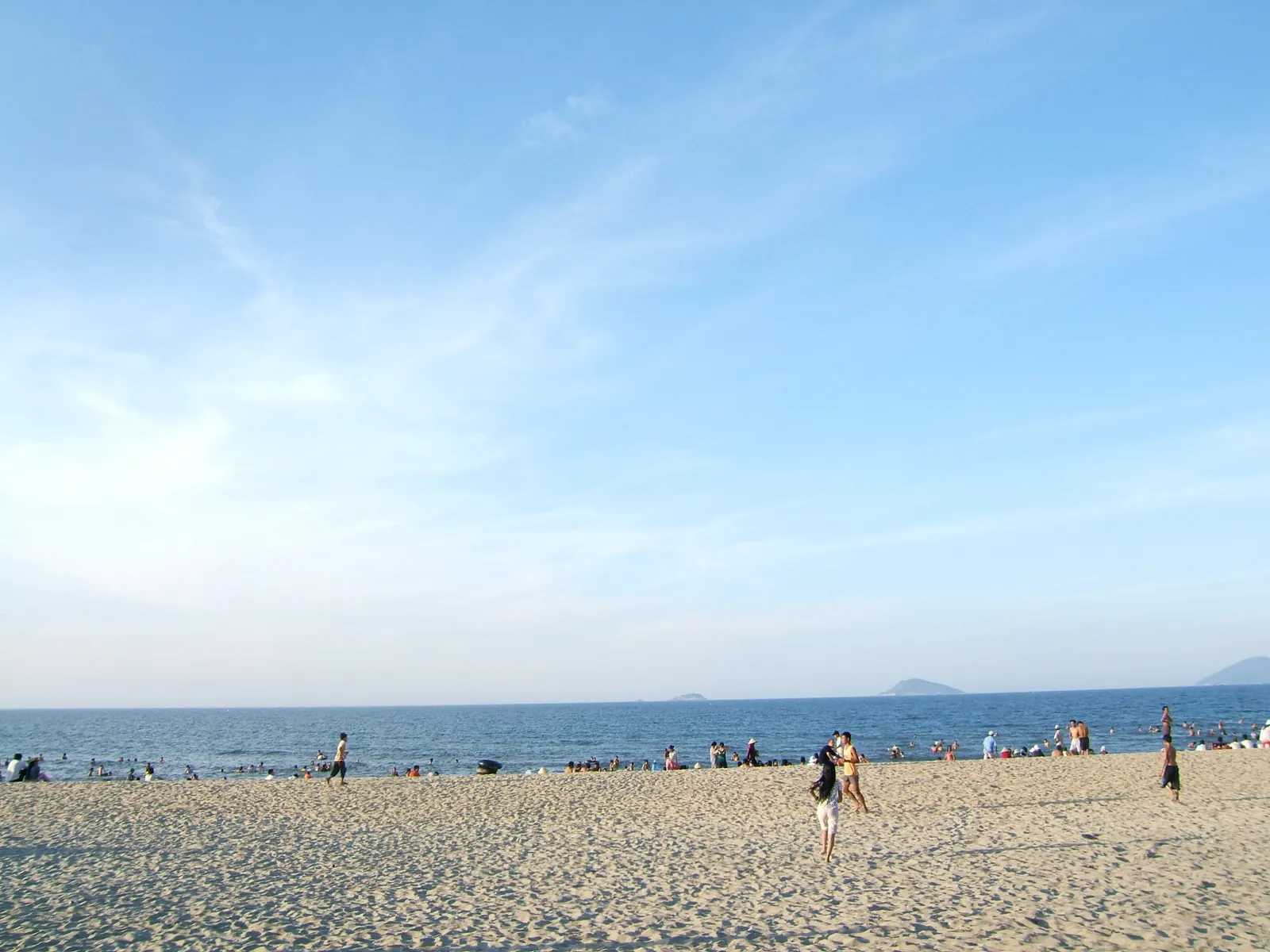 Badgäster på den breda sandstranden Cua Dai vid Hoi An med Chamöarna vid horisonten
