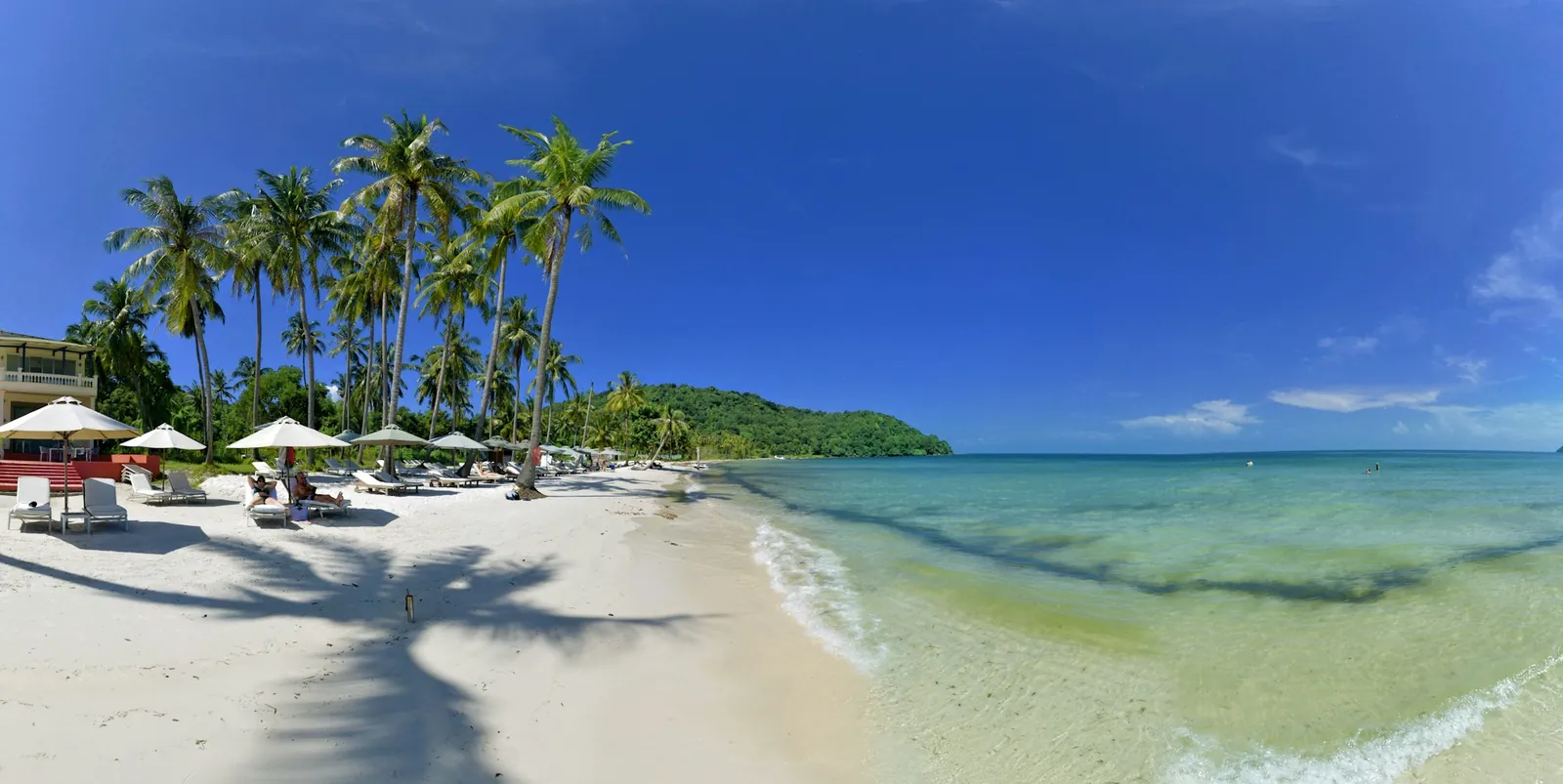 Kokospalmer, parasoller och vit sand vid turkost vatten på Sao-stranden på ön Phu Quoc