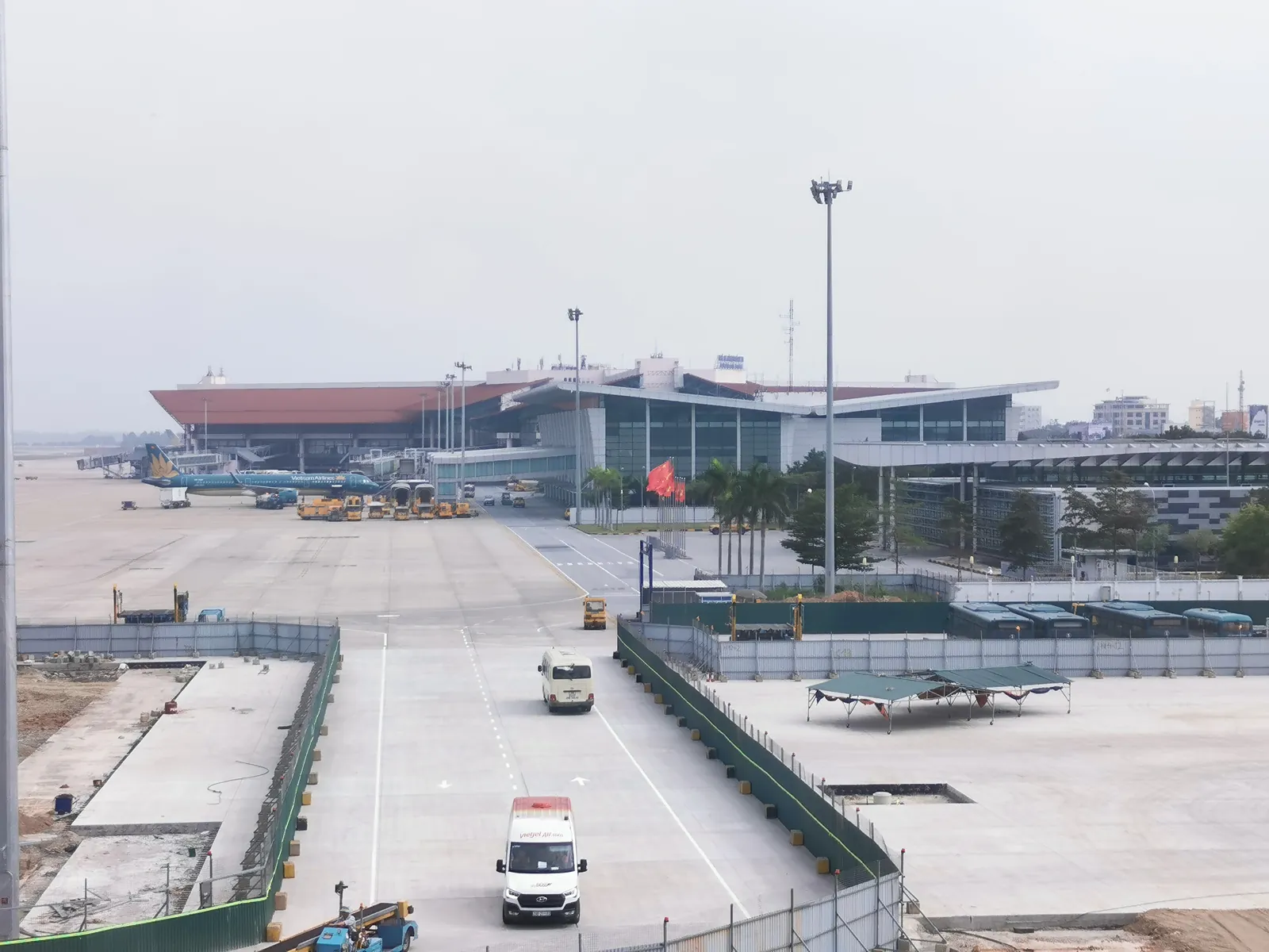 Inrikesterminalen på Noi Bai med flygplan vid gaterna, vietnamesiska flaggor och väntande bussar